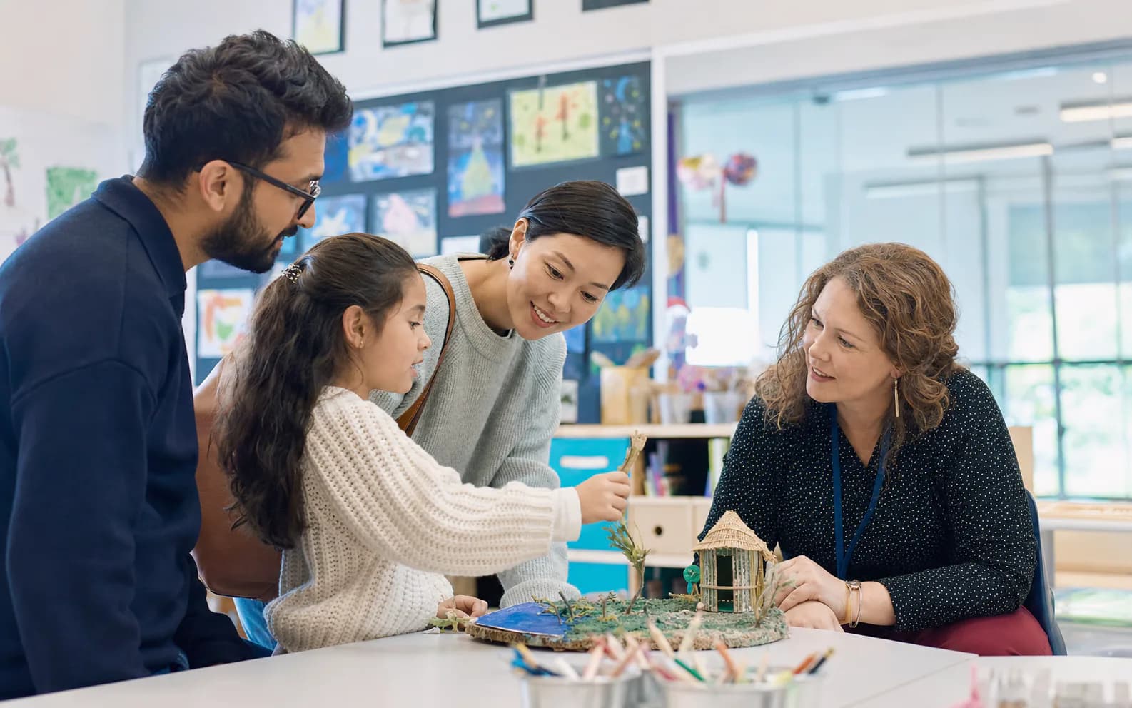 A primary student sharing a classroom project with family members and her teacher