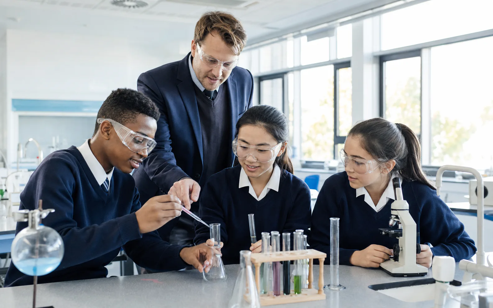 Three secondary students and a teacher collaborating safely on a chemistry investigation